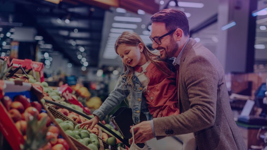 A father holding his daughter pick out fresh produce at the store